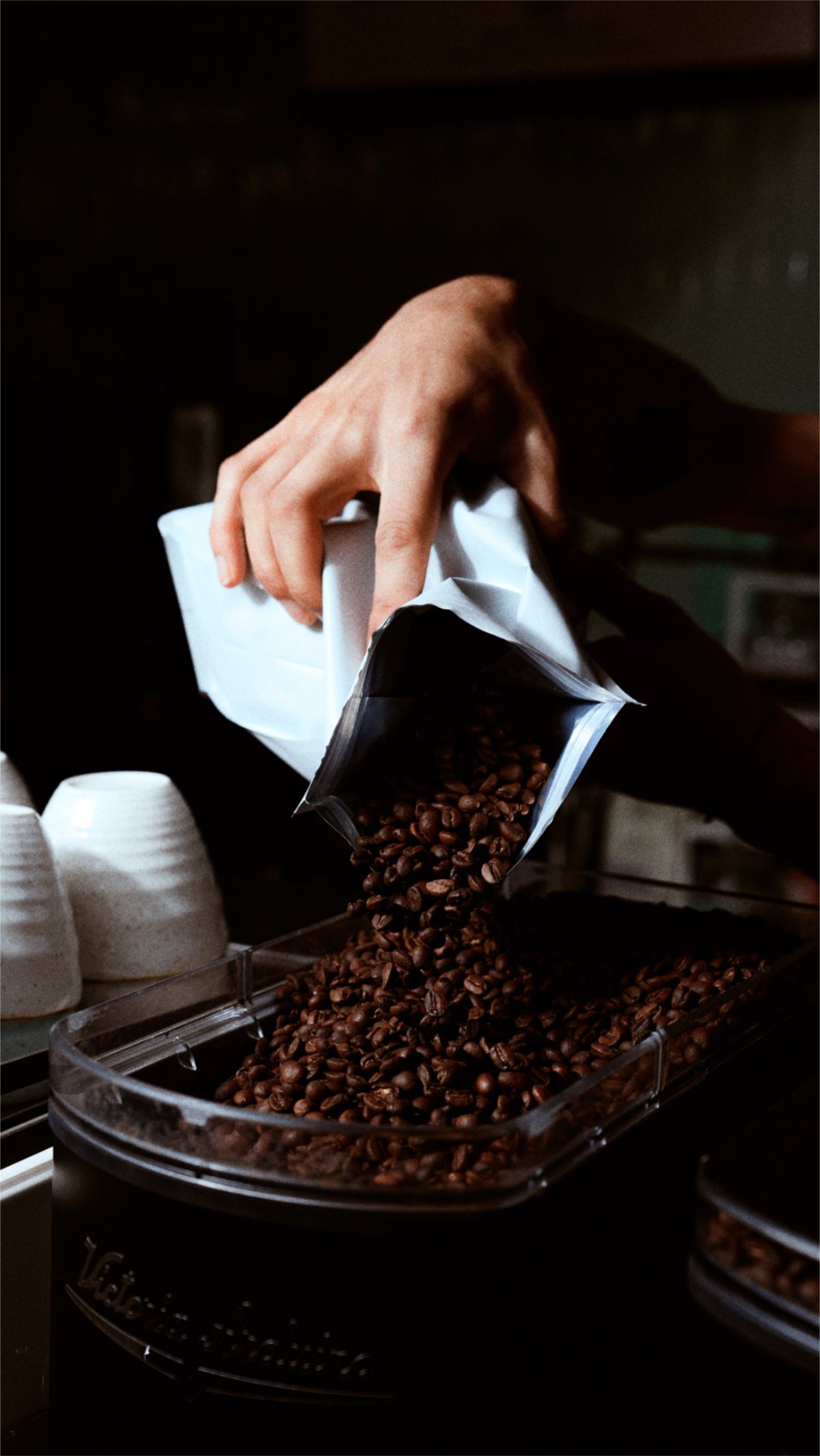 Hand pouring coffee beans from a bag into a container.